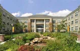 An apartment building with a grass field and rocky landscaping in front of it.