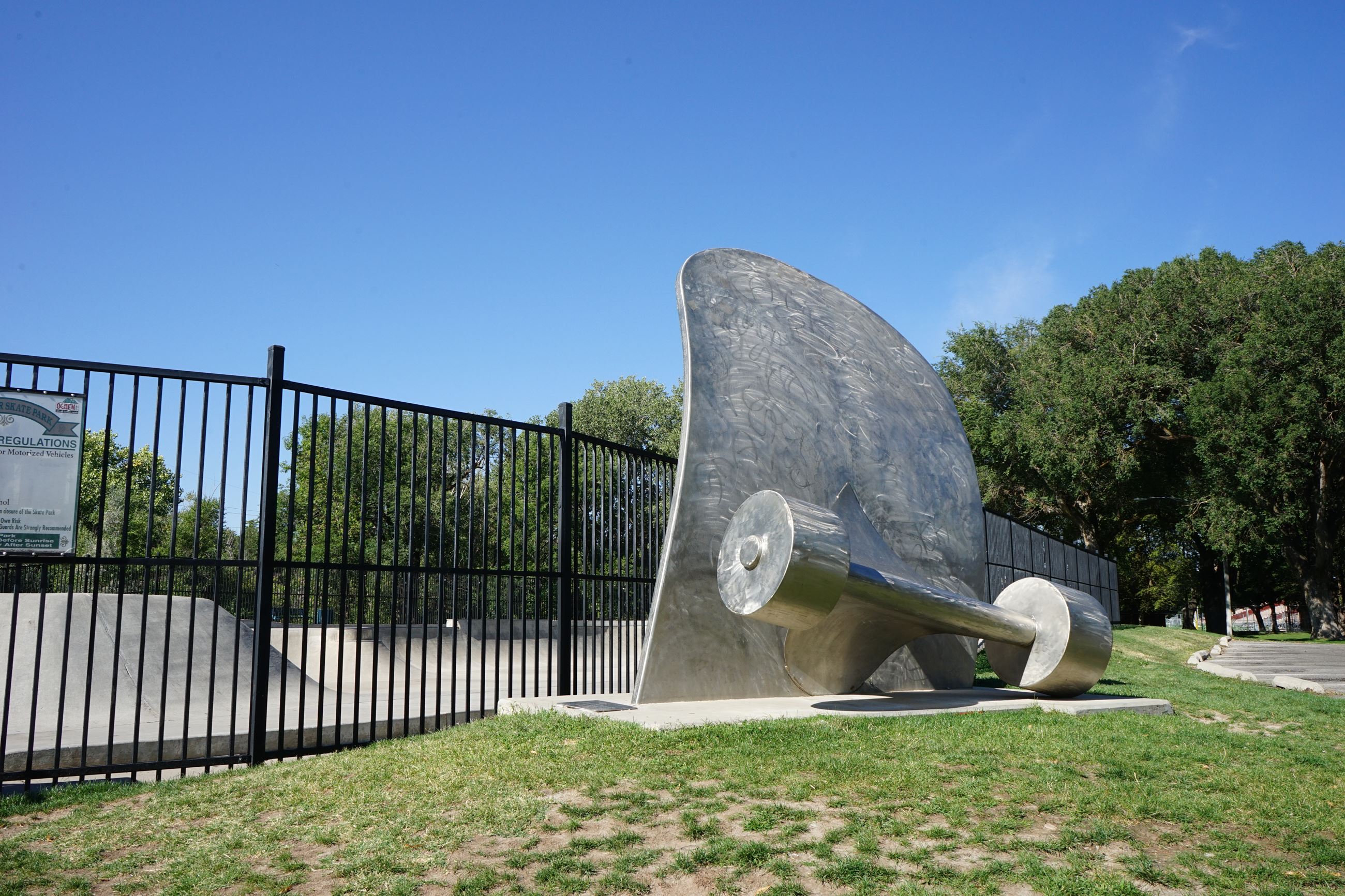The outside of a skate park with a metal statue of a skate board going into the ground